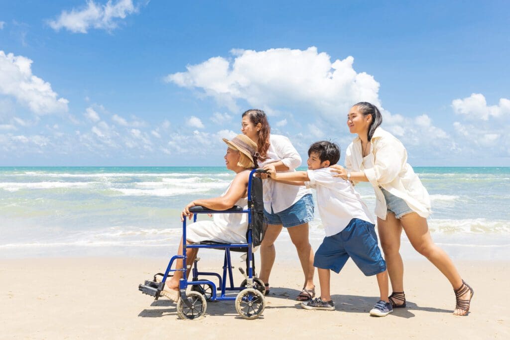 Family pushing a loved one in a wheelchair on a beach